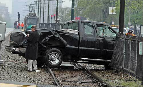 Workers (right) tried to remove and repair fencing that was damaged when this pickup truck was pushed across the MBTA tracks. In the background, a green line trolley idled.