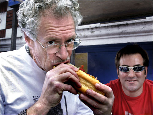 Chef Jasper White eats sausage while working the stand of Sausage Guy David Littlelfield on Landsdown St.
