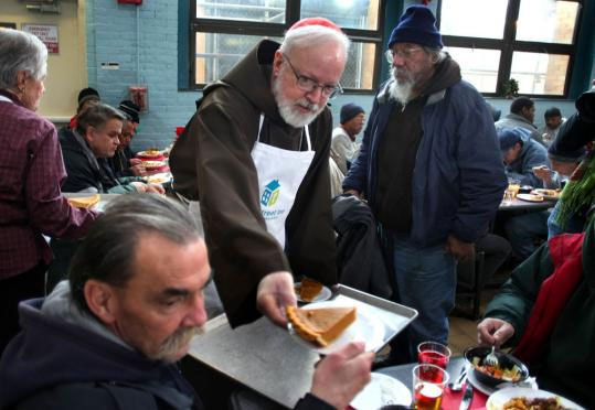 Cardinal Sean P. O’Malley helped serve a slice of pie during a Christmas Eve lunch for homeless men and women at the Pine Street Inn. He said it has been a tough year for those less fortunate.