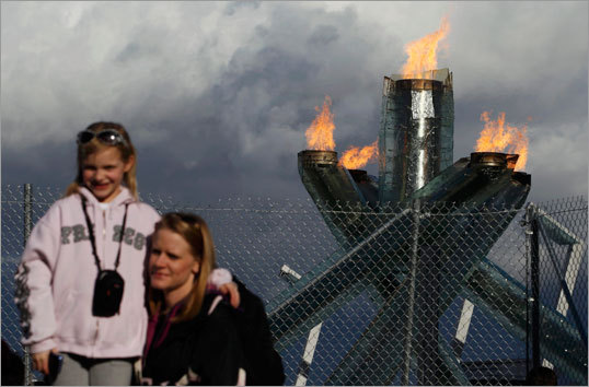Spectators posed in front of the Olympic cauldron, which is kept behind a chain link fence.
