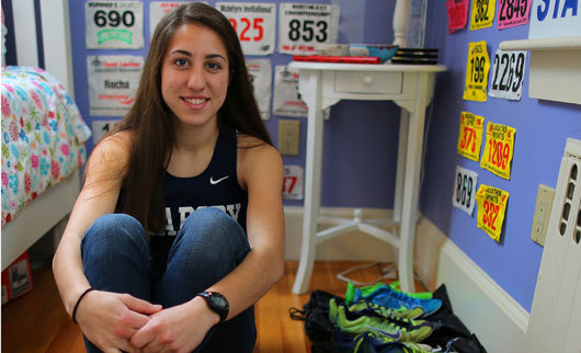 Catarina Rocha sits beside a row of running shoes, with her running bibs in the backdrop.