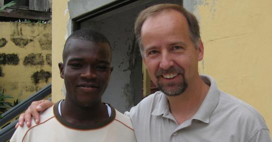 Babson College dean Dennis Hanno stands with Benjamin, a resident of Sekondi, Ghana, who has gone from being an apprentice of a furniture maker to owner of a manufacturing business with four employees, after taking business-training courses provided by Hanno and his students.