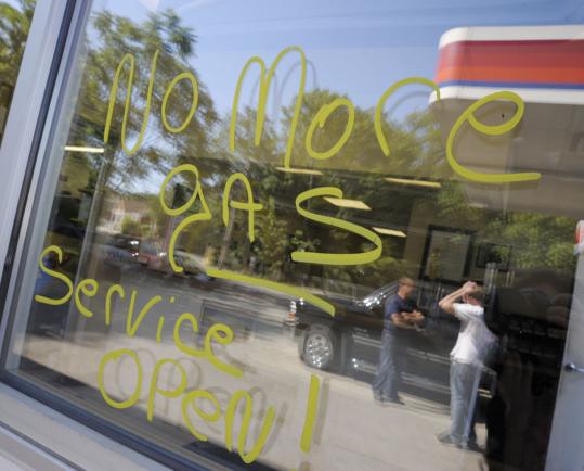 A window at Sutton Street Service in North Andover showed the reflection of owner Chip McAllister (left) and a customer. The writing on the window says the station no longer sells gas.