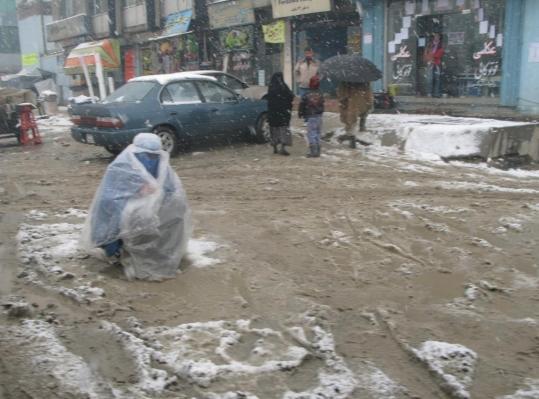 Wearing a burqa and a plastic sheet, a woman begged on a Kabul street. Afghanistan remains one of the poorest countries, with high rates of unemployment, illiteracy, and infant mortality.