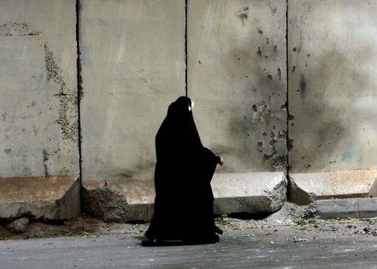 Iraqi women walked past walls scarred by a detonated roadside bomb that targeted a police patrol in the Karada district of Baghdad yesterday. One person died in the blast.