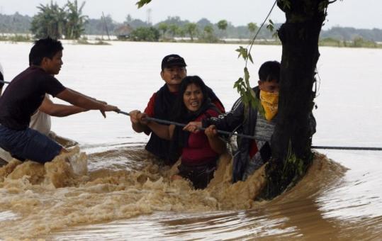 Residents held onto a rope yesterday while crossing a highway flooded by heavy rains in a town north of Manila.