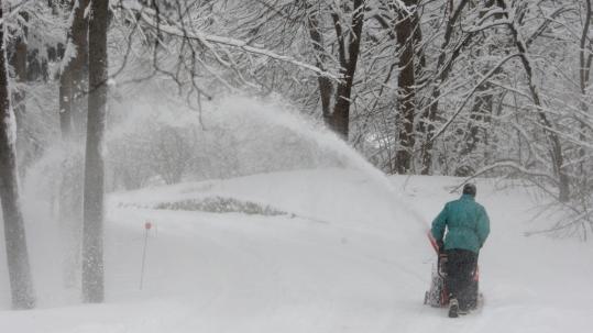In Hamilton yesterday, Jim Dooley used a snow blower to clear his driveway. Persistent snowfall could mean about 6 to 10 inches of accumulation in many counties.