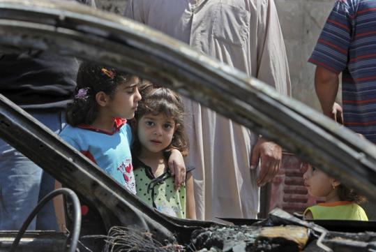 Children stood near a destroyed vehicle in Baghdad yesterday. Bombs  targeting Shi’ite mosques around Baghdad killed 72 Friday.