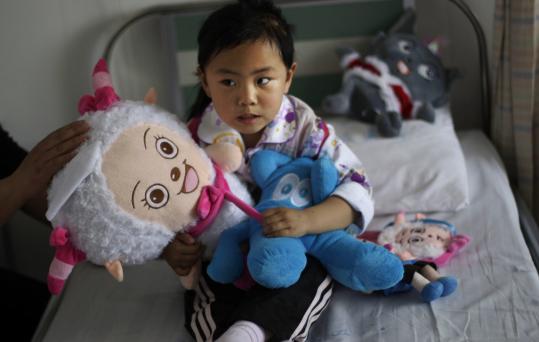 A girl who  was attacked played with her toys at a hospital in Taixing, China.  Police and security guards patrolled the lobby of the hospital the  morning after marching parents protested.