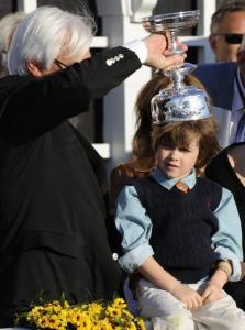 Lookin At Lucky trainer Bob Baffert, who won his fifth Preakness Saturday, places the trophy on the head of son Bode.