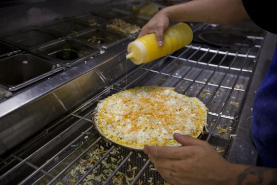 A Domino’s Pizza employee made one of the chain’s Wisconsin six-cheese pizzas in New York. Cheese has become the largest source of saturated fat in the American diet.
