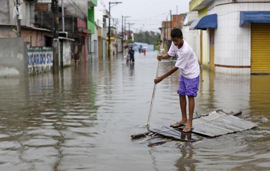 A youth used a makeshift raft yesterday to cross a flooded street in the Vila Itaim neighborhood of Sao Paulo.