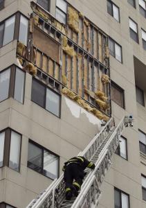 A firefighter made his way down the ladder after inspecting the wind-damaged facade of the 10-story Olympia Tower residence in New Bedford yesterday.